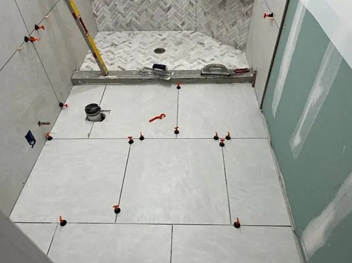 Instalación de pavimento cerámico en un plato de ducha integrado, empleando cuñas de nivelación y sistemas de separación técnica para asegurar el drenaje.