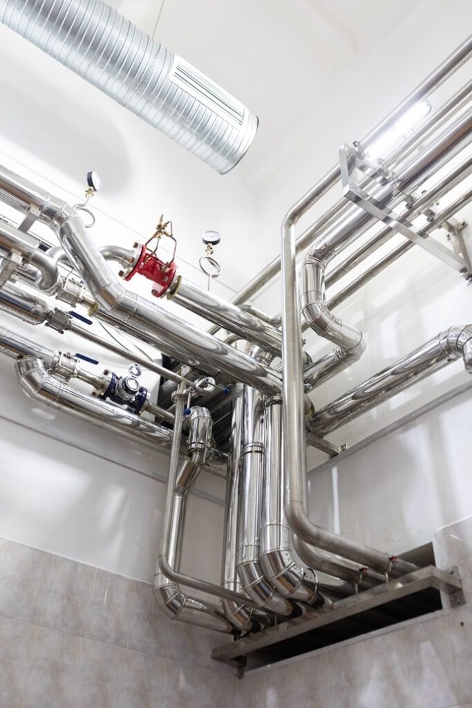 Detalle técnico de un intercambiador hídrico de acero inoxidable con valvulería y manómetros en una sala de máquinas hotelera.